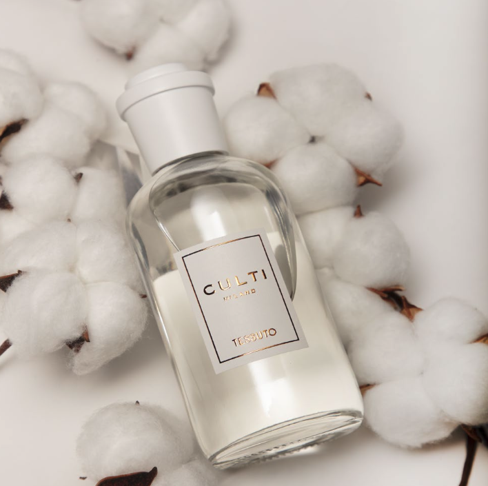 Un flacone trasparente Culti Milano TESSUTO è adagiato tra soffici capsule di cotone bianco su fondo chiaro, con un'atmosfera elegante e delicata.