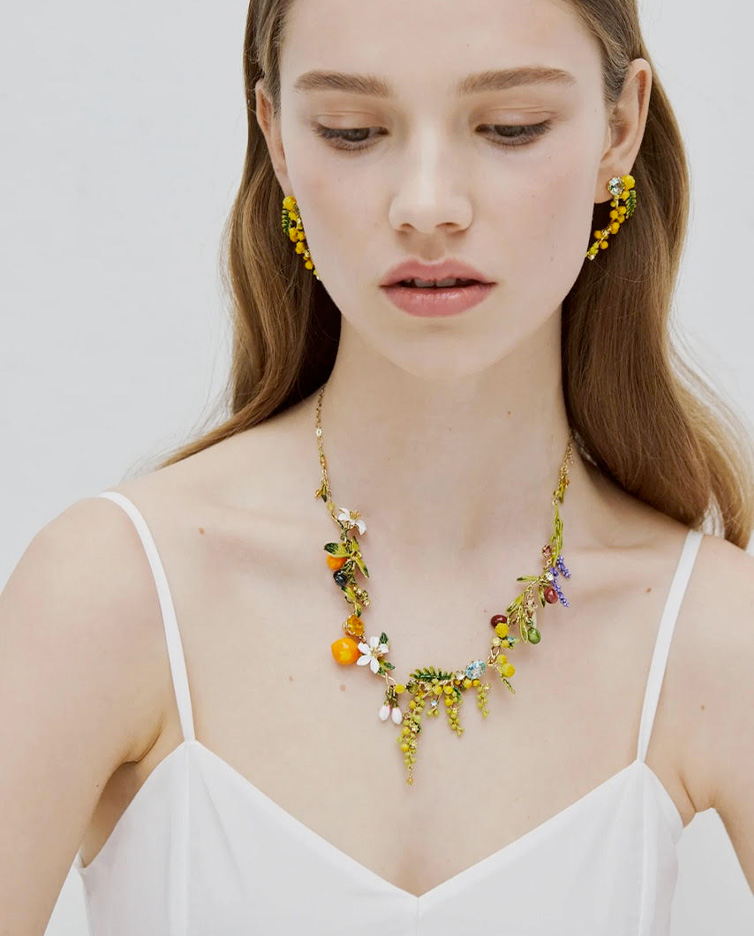 Collana e orecchini Les Nereides con dettagli floreali e fruttiferi indossati da una giovane donna.