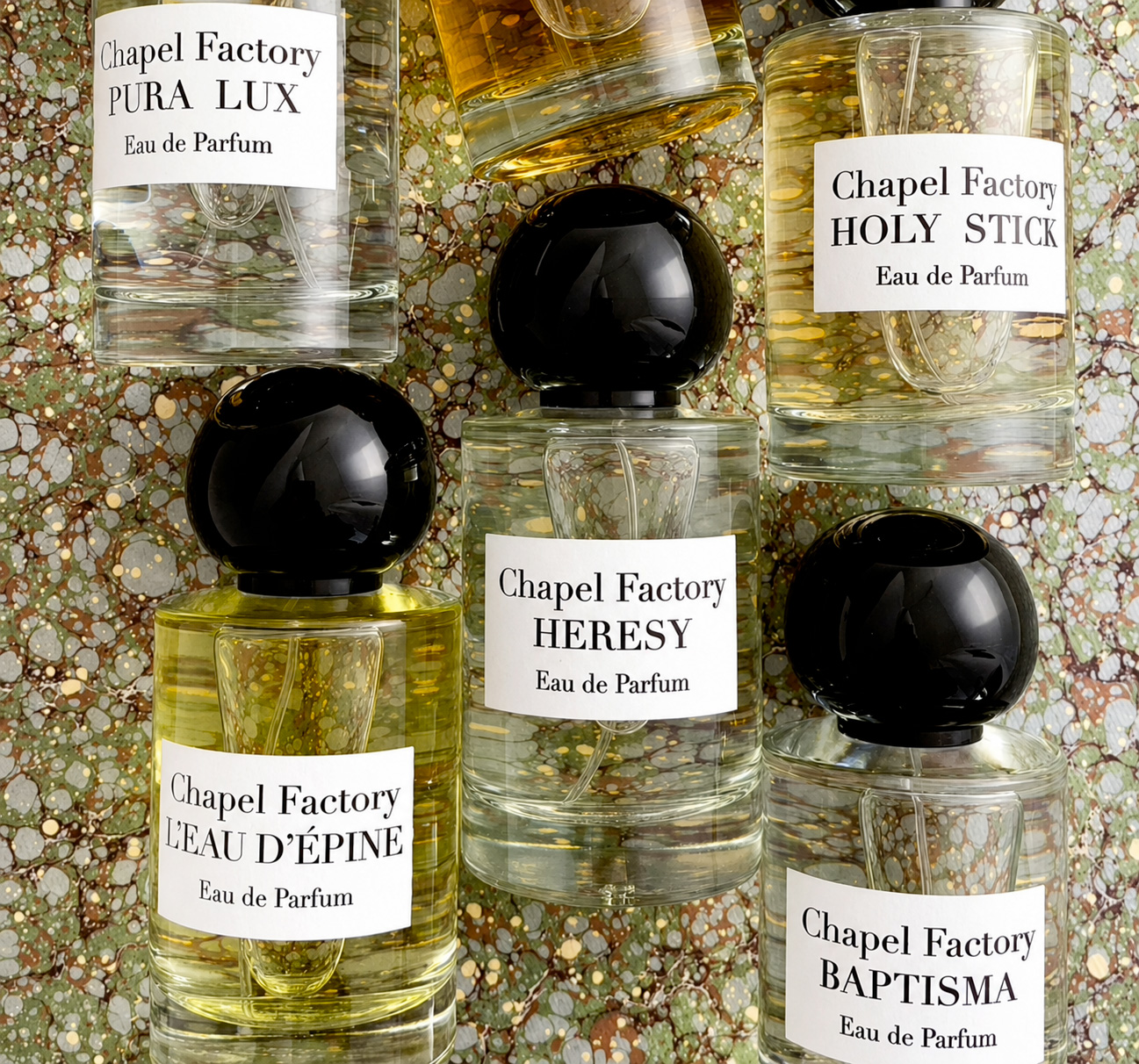Cinque flaconi di profumo Les Cocottes Paris con etichette dorate sono disposti su fondo beige, con nomi come La Belle Otero e Cora Pearl.