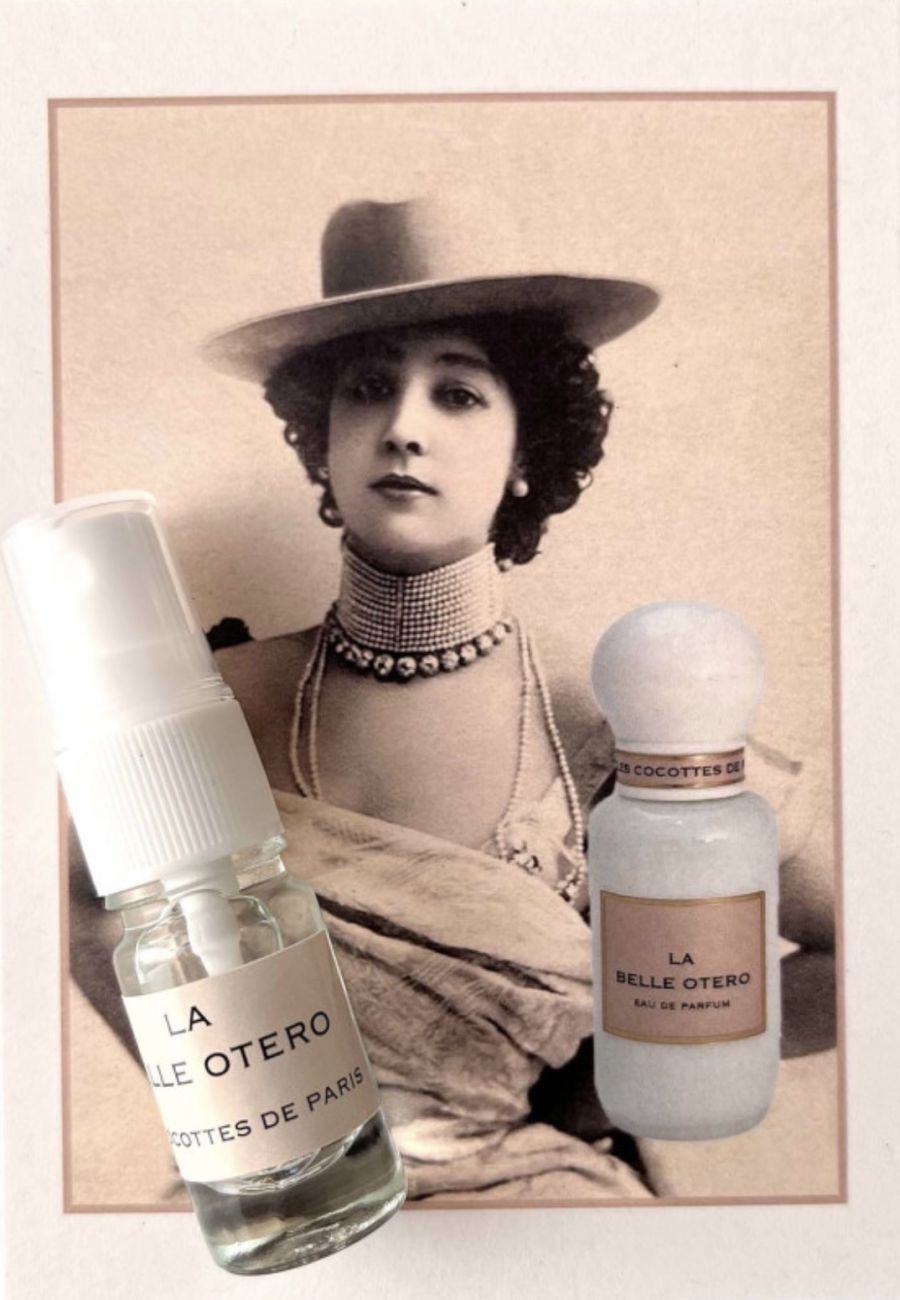 Un ritratto vintage in seppia di La Belle Otero con cappello a tesa larga, gioielli e due flaconi di profumo sovrapposti in primo piano.